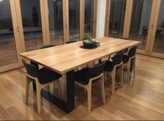 a wooden table surrounded by black chairs in a room with wood floors and glass doors