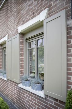 two planters on the side of a brick building with green shutters and white trim