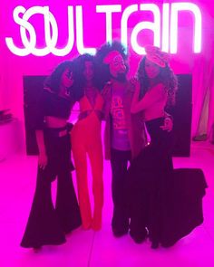 three women standing in front of a neon sign with the word soul train on it