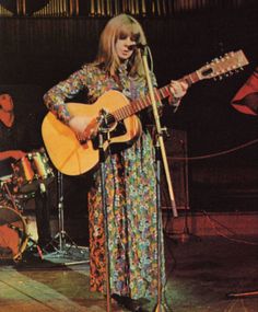 a woman standing in front of a microphone while holding a guitar