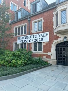 a welcome sign is posted in front of a large brick building with windows and doors