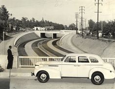 an old black and white photo of a man standing next to a car on the road