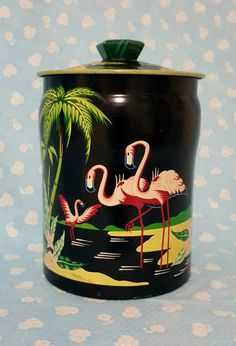 a black canister with pink flamingos and palm trees painted on the side, sitting on a blue background