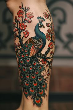 a peacock tattoo on the back of a woman's leg with red flowers and leaves