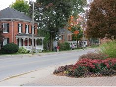 an old brick house on the corner of a street with trees and bushes around it