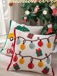 two christmas pillows sitting on top of a bed next to a christmas tree with stockings and stocking