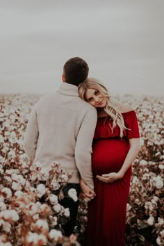 a pregnant woman in a red dress standing next to a man in a field of cotton