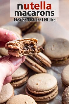 a hand holding an open nutella macarons in front of a pile of cookies