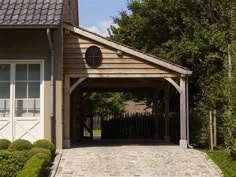 a house with a brick driveway and covered garage area in the front yard, surrounded by greenery