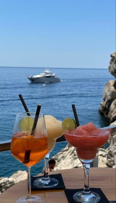 two drinks sitting on top of a wooden table next to the ocean