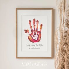 a framed hand print hangs on the wall next to some dry grass and a plant