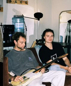 two people sitting on a couch with guitars in their hands and one person holding an electric guitar