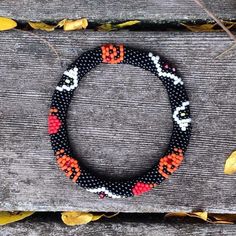 a black beaded bracelet with orange and white beads sits on top of a wooden bench