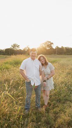 a man and woman are standing in the middle of an open field at sunset, posing for a photo