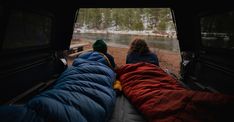 two people sitting in the back of a truck with their sleeping bags on top of them