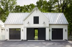 two garages in front of a white house with black doors and windows on each side