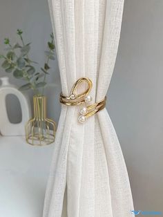 a white curtain with gold rings and pearls on the side, next to a vase