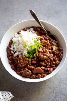 a white bowl filled with beans and rice on top of a gray table next to a spoon