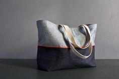 a gray and orange tote bag sitting on top of a black table next to a white wall