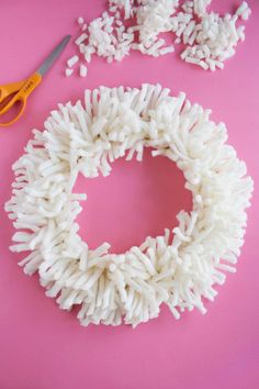 a pair of scissors sitting next to a wreath made out of white rice on a pink surface