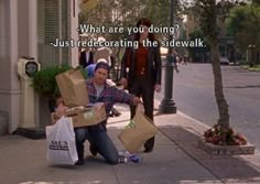 a man sitting on the sidewalk with two boxes in front of him and another person standing next to him