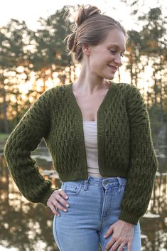 a woman standing in front of a body of water wearing a green cardigan sweater