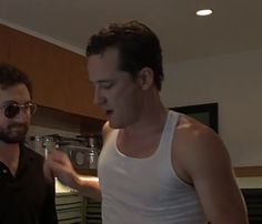 two men standing next to each other in a kitchen