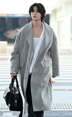 a woman walking down the street carrying a handbag in her right hand and wearing a gray coat