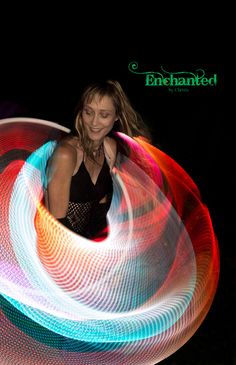 a woman in a black top is spinning a colorful light up hula hoop around her