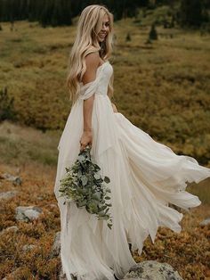 a woman in a white dress holding a bouquet on top of a hill with grass and rocks