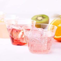 several glasses filled with different colored liquid next to an orange and kiwi