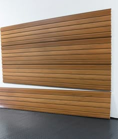 a wooden slatted wall next to a white wall with black flooring on it