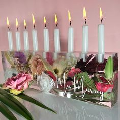 a group of white candles sitting next to each other on top of a table with flowers