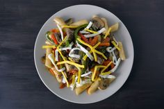 a white plate topped with pasta covered in cheese and vegetables on top of a wooden table