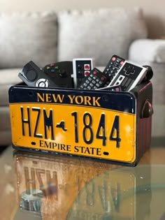 a yellow license plate with remotes in it sitting on a table next to a couch