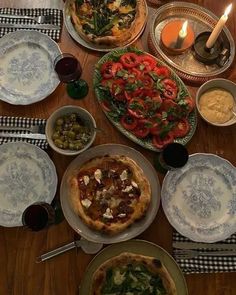 a wooden table topped with plates and bowls filled with different types of food next to candles