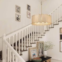 a white staircase with pictures on the wall and a chandelier hanging above it