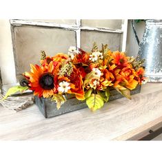 an arrangement of sunflowers and other flowers in a metal container on a table