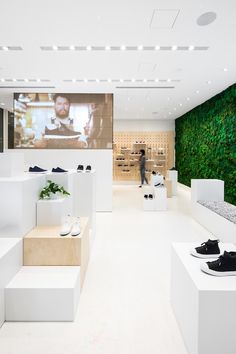 the interior of a shoe store with white walls and green plants on the wall behind them