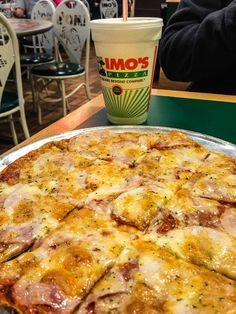 a large pizza sitting on top of a pan next to a cup of coffee in a restaurant