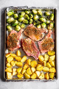 raw pork chops, potatoes and brussel sprouts on a baking sheet