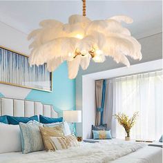 a white bed sitting under a chandelier in a bedroom next to a window