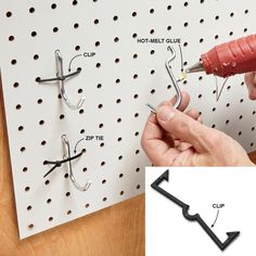 a person is holding a screw and pointing to some clips on a pegboard that are attached to the wall