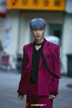 a young man with blue hair wearing a purple suit and black shirt standing in front of a building