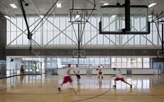 some people are playing basketball in an indoor court with lights on the ceiling and windows