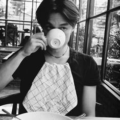 a woman sitting at a table drinking from a cup