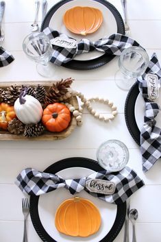 the table is set with black and white plates, silverware, and pumpkins