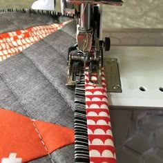 a close up of a sewing machine with an orange and white quilt on it's side