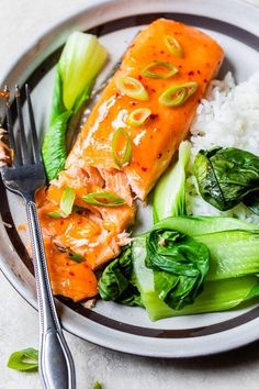 a plate with salmon, rice and greens on it next to a knife and fork