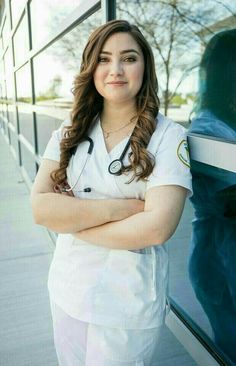 a woman in white scrubs is leaning against a glass wall with her arms crossed